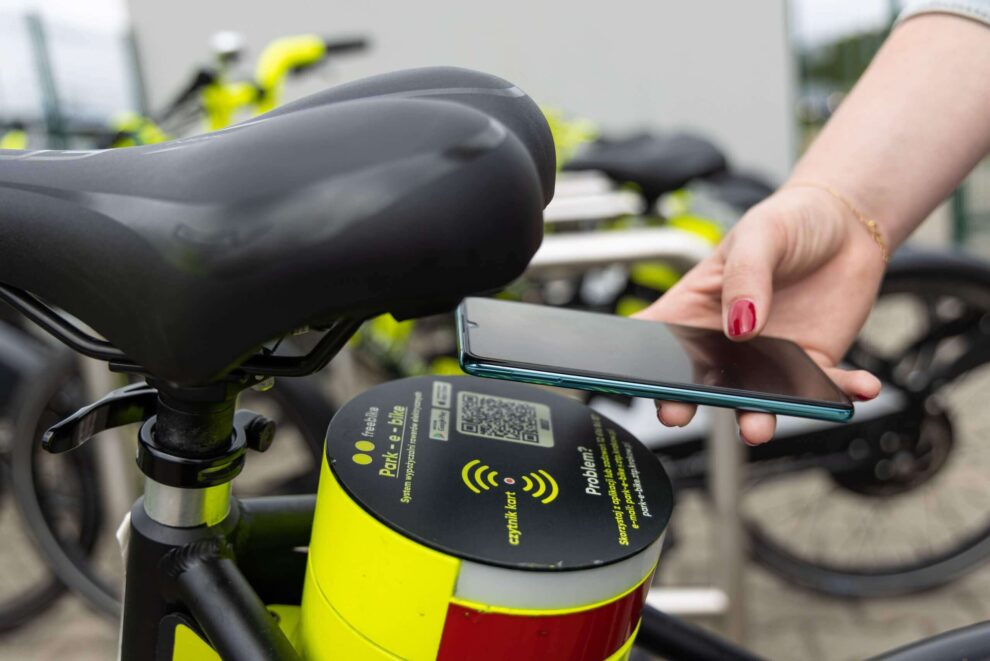 Zdjęcie przedstawia skanowanie telefonem QR kodu umieszczonego za siodełkiem roweru elektrycznego w celu wypożyczenia go w systemie park-e-bike